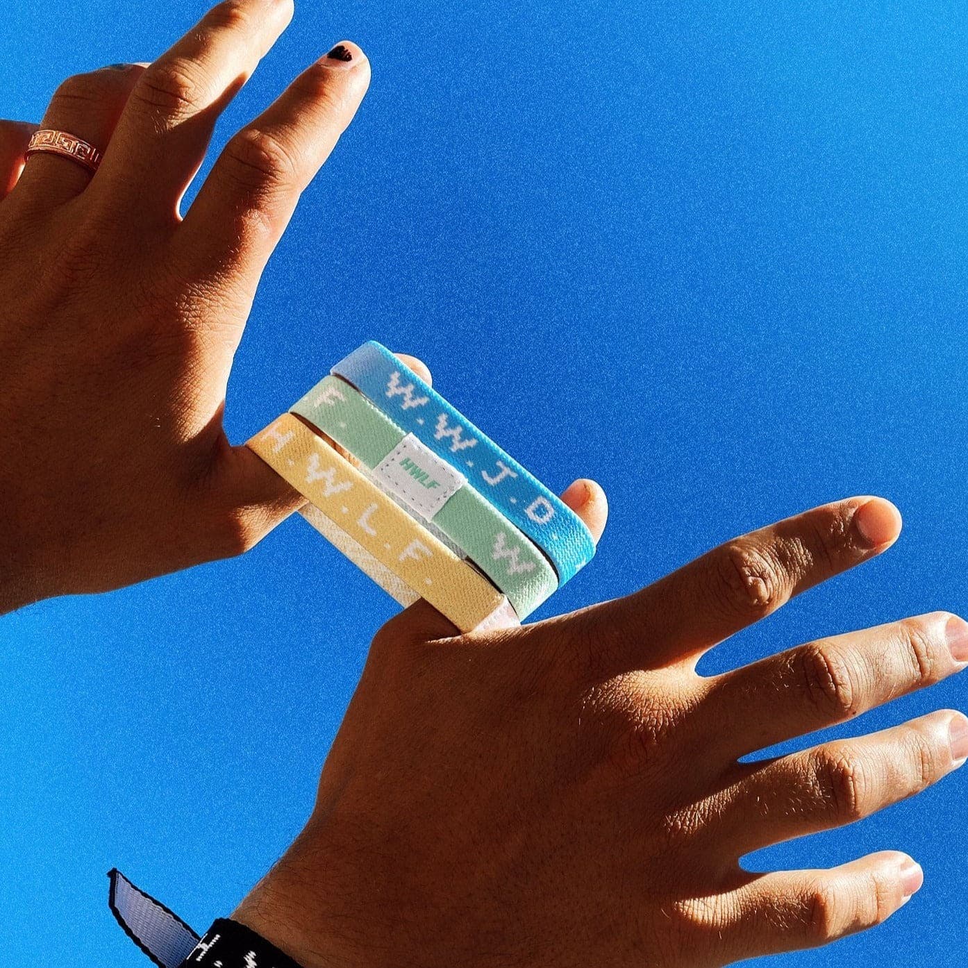 WWJD x HWLF pastel elastic 3-pack held up against a blue sky